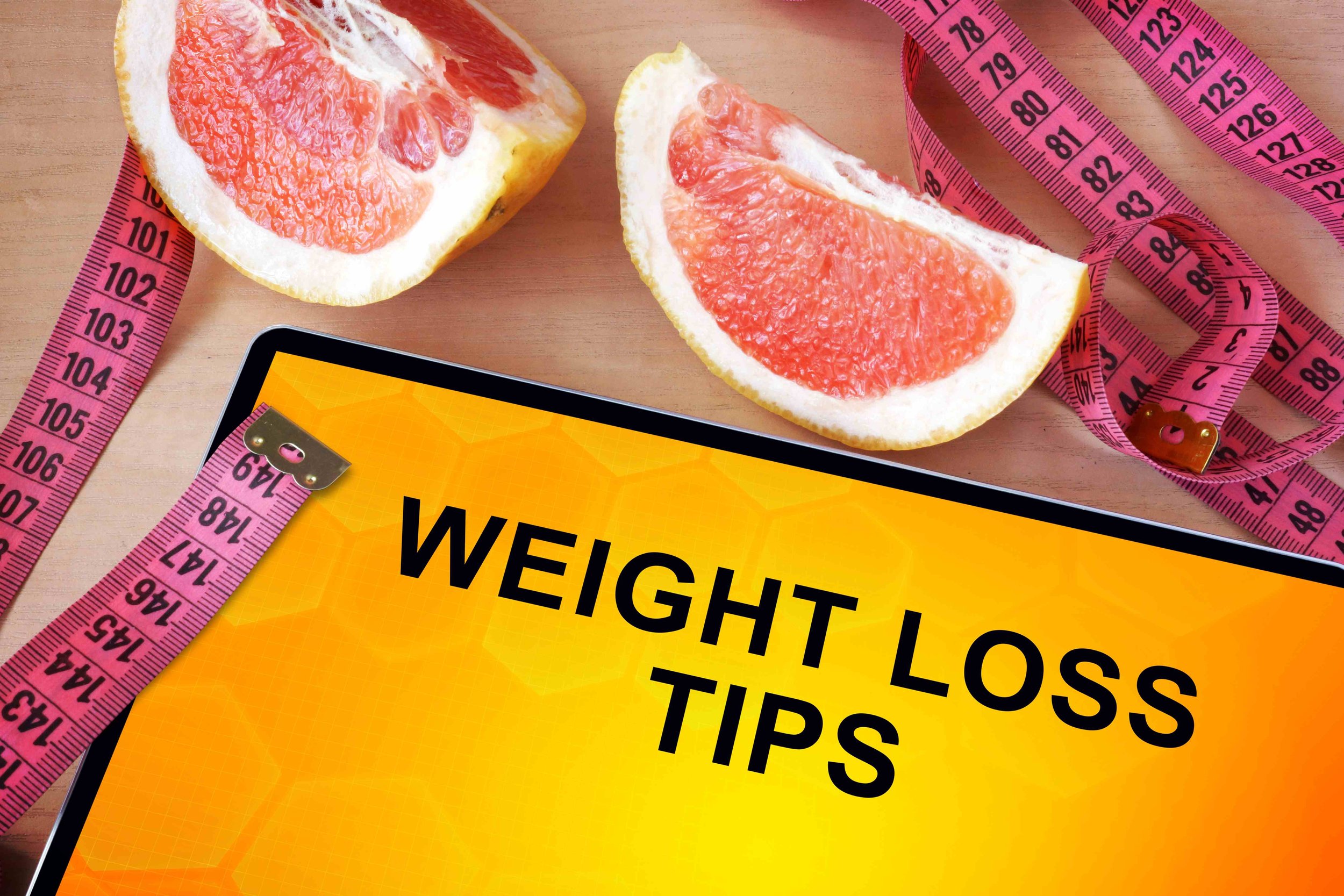 Healthy weight loss foods including avocado, berries, eggs, salmon, chia seeds, and green tea on a white wooden table